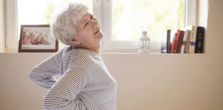 Older woman sitting and holding her lower back in pain