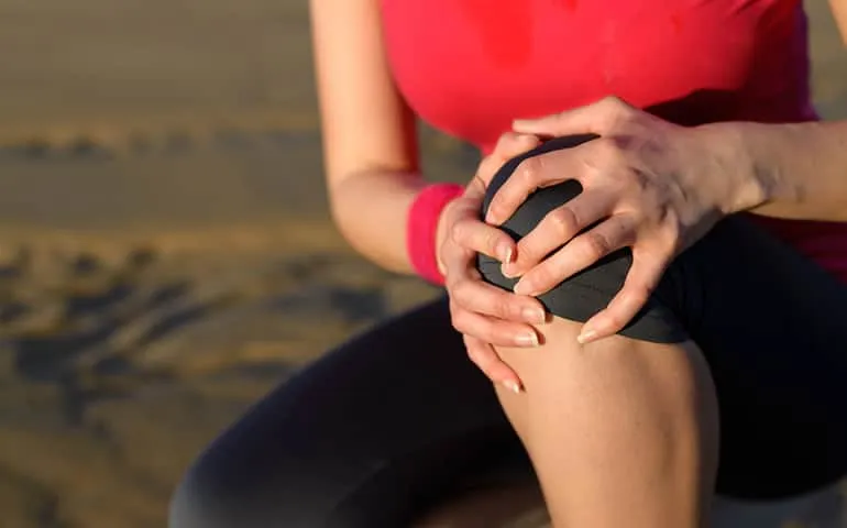 Person holding their knee outdoors with a highlighted area of pain