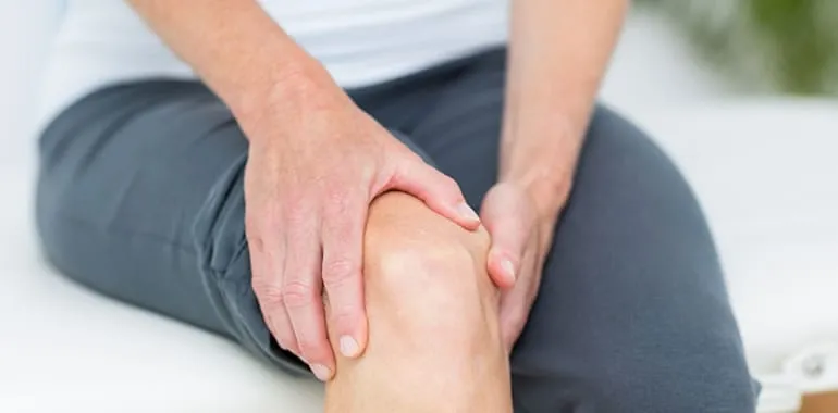 Close-up of hands holding a knee in pain