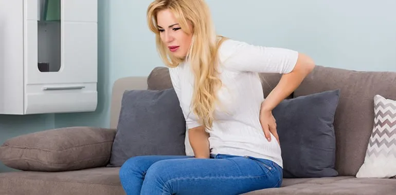 Woman sitting on a couch holding her lower back in pain